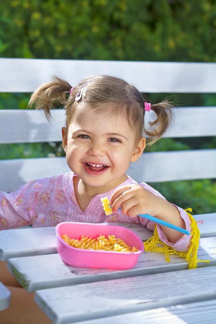 Little girl eating pasta in garden