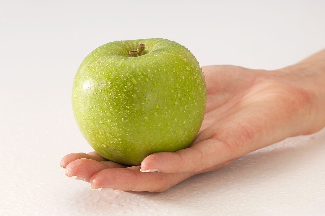 Hand holding green apple with drops of water