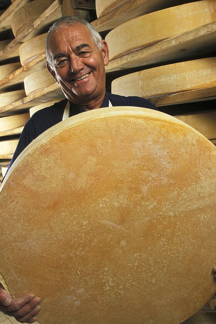A man holding a large wheel of cheese (Comte)