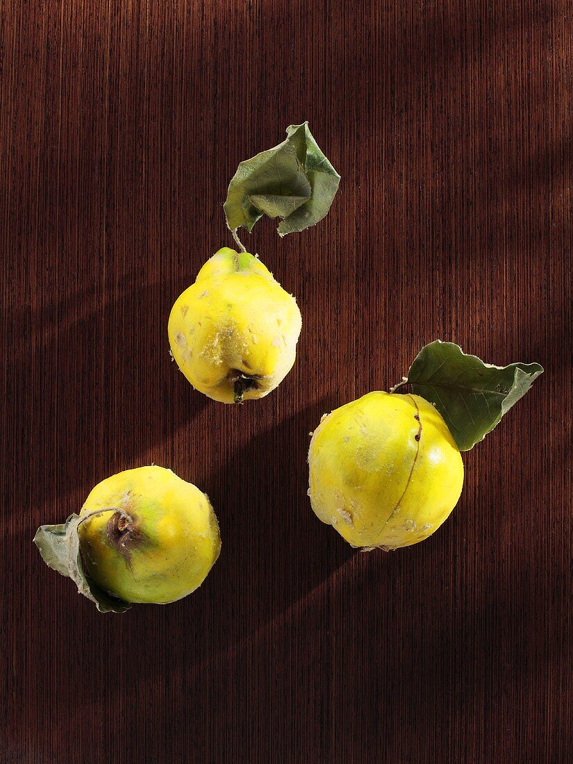 Three quinces with leaves on wooden background (overhead view)