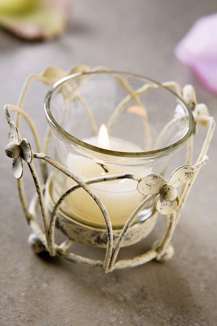 Tealight in glass on stone surface with rose petals