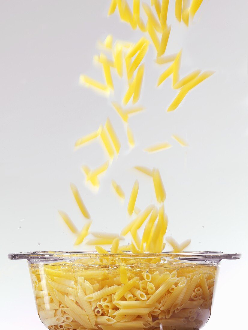 Penne falling into water in glass pot