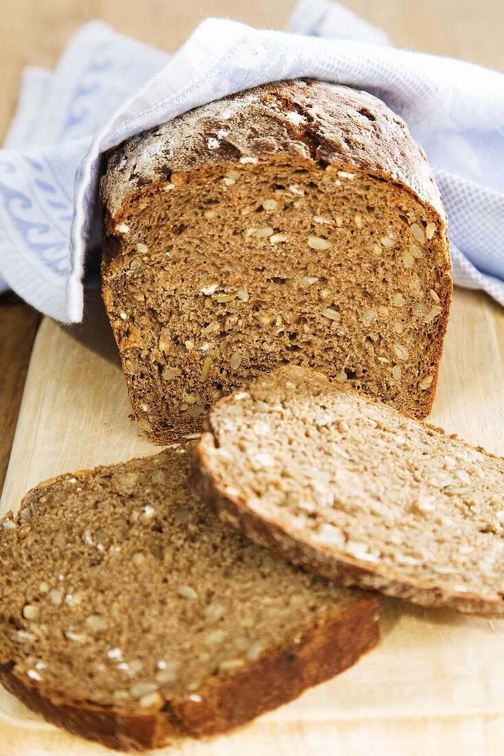 Roggenvollkornbrot, angeschnitten, auf Schneidebrett mit Tuch