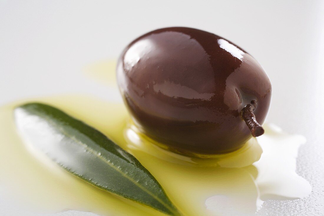 Schwarze Olive mit Olivenöl und Olivenblatt (Nahaufnahme)