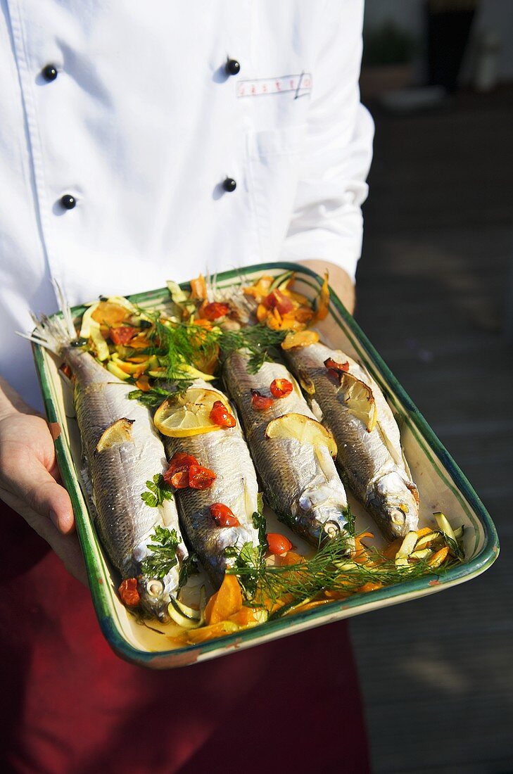 Koch hält gebratene Fische mit Zitronen, Gemüse und Dill