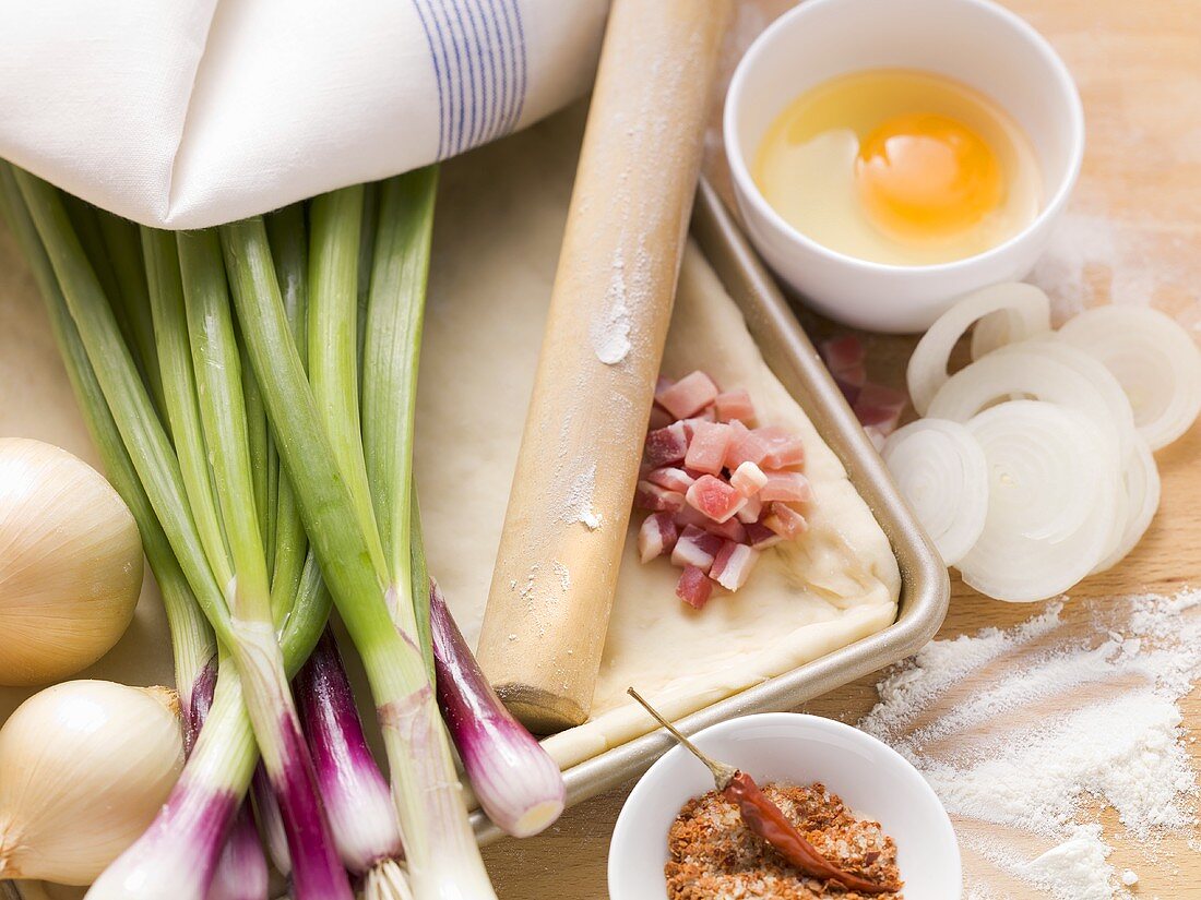 Ingredients for tarte flambée: spring onions, diced bacon, yeast dough, egg
