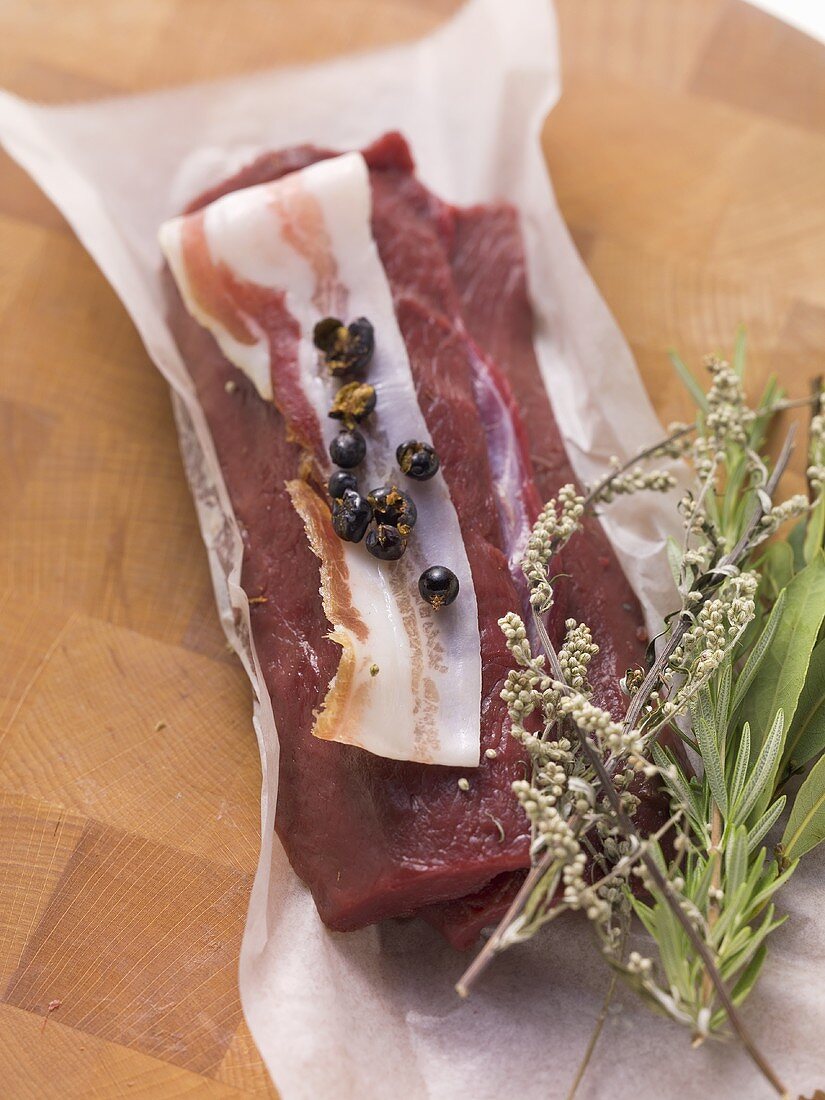 Venison fillet with slice of bacon and herbs