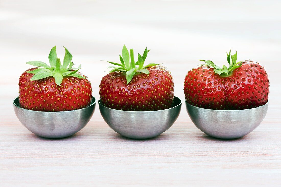 Three strawberries in small metal dishes