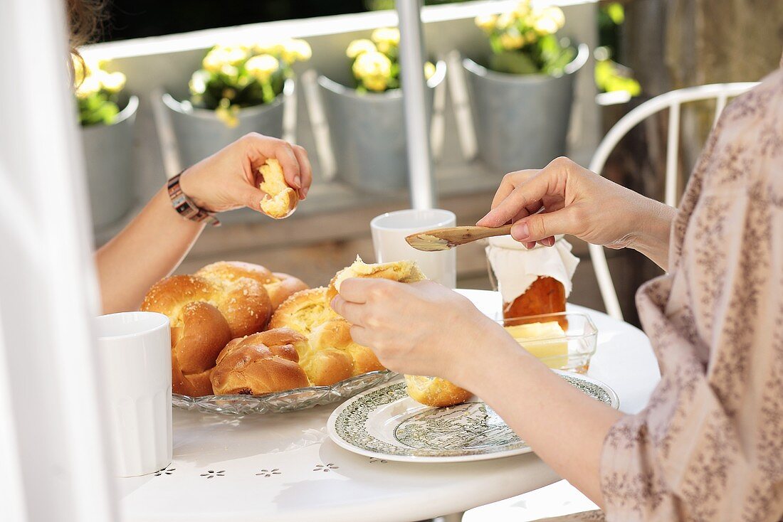 Two women eating a Hefezopf (sweet bread from southern Germany) for breakfast on the terrace