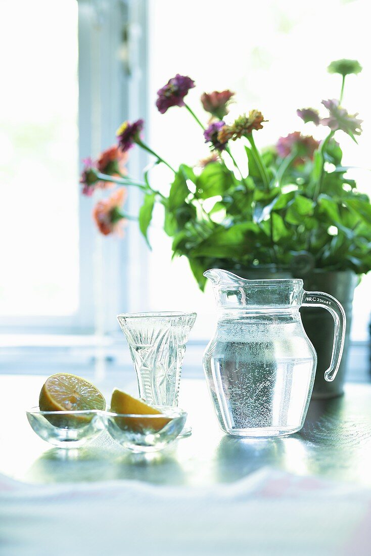 A jug of water, lemons and flowers on a table