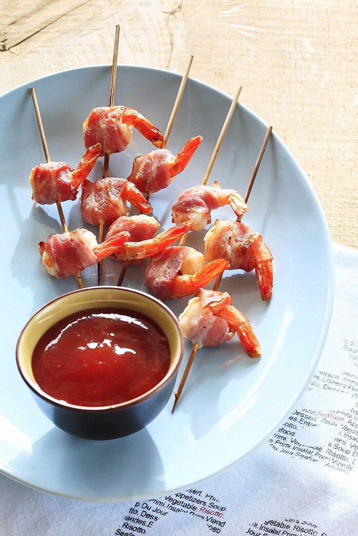 Barbecued bacon-wrapped prawns on wooden skewers, ketchup