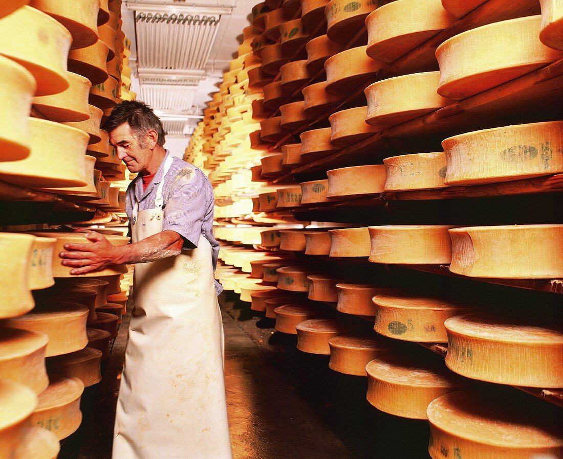 Man turning cheeses on wooden shelves