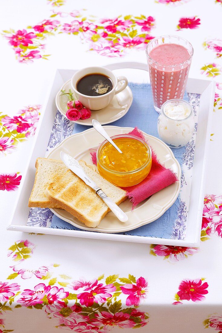 Frühstückstablett mit Toast, Orangenmarmelade, Quark, Kaffee und Erdbeersmoothie