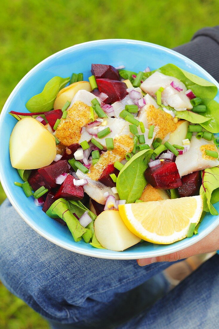Person holding bowl of salad (beetroot, herring, potatoes)