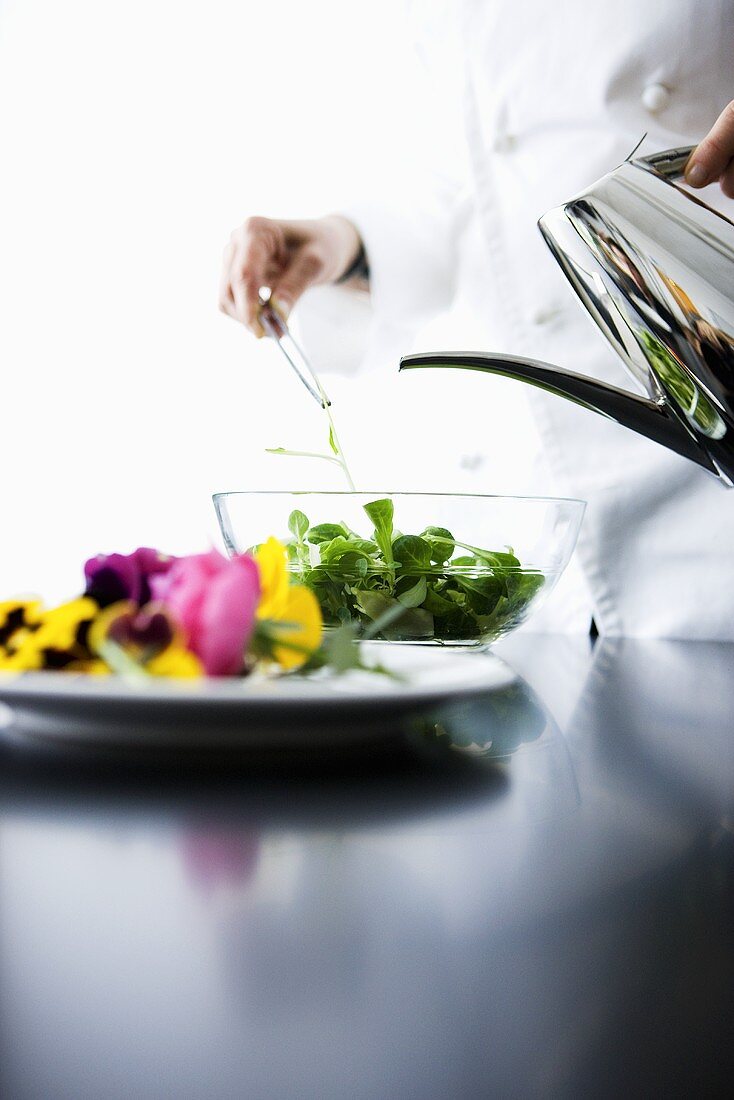 A chef pouring oil over a mixed leaf salad
