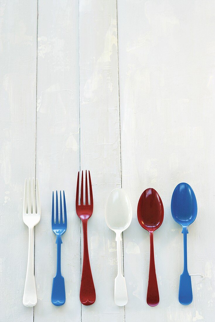 Different coloured forks and spoons on wooden background