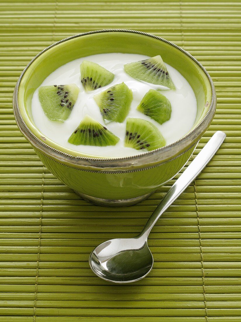 Naturjoghurt mit Kiwis in grüner Schale, daneben Löffel