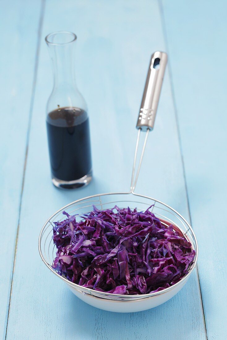 Cooked red cabbage in a sieve with balsamic vinegar in the background