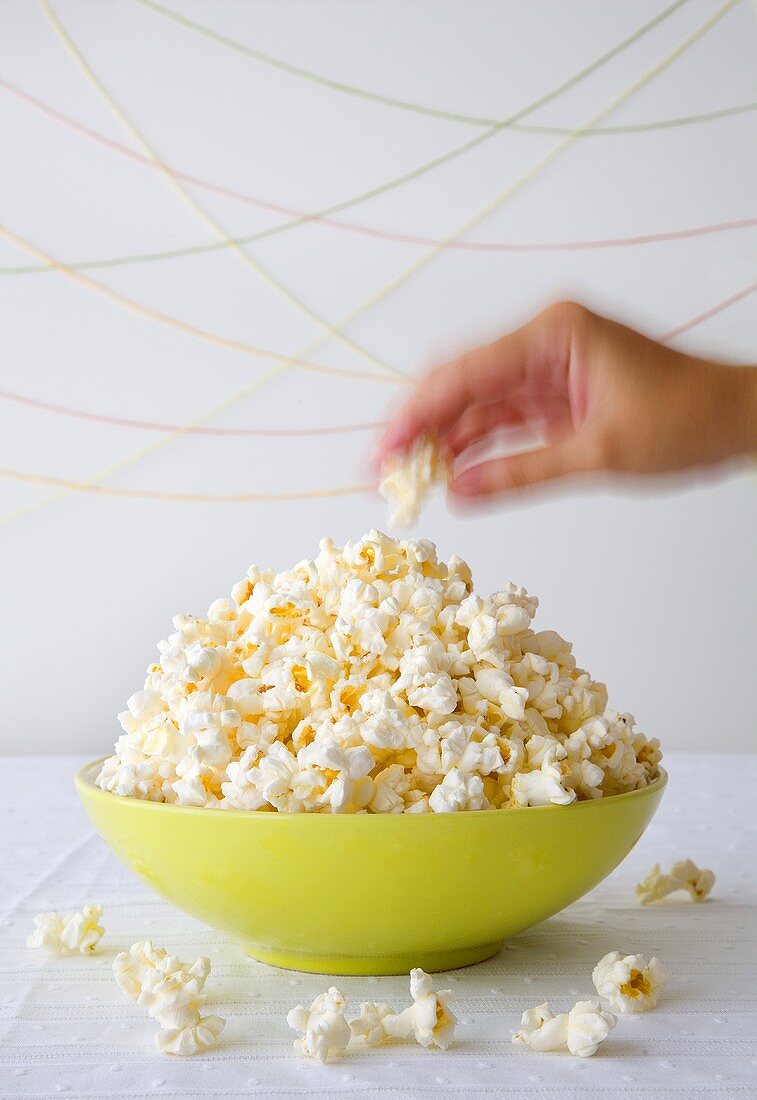 A hand taking popcorn out of a bowl
