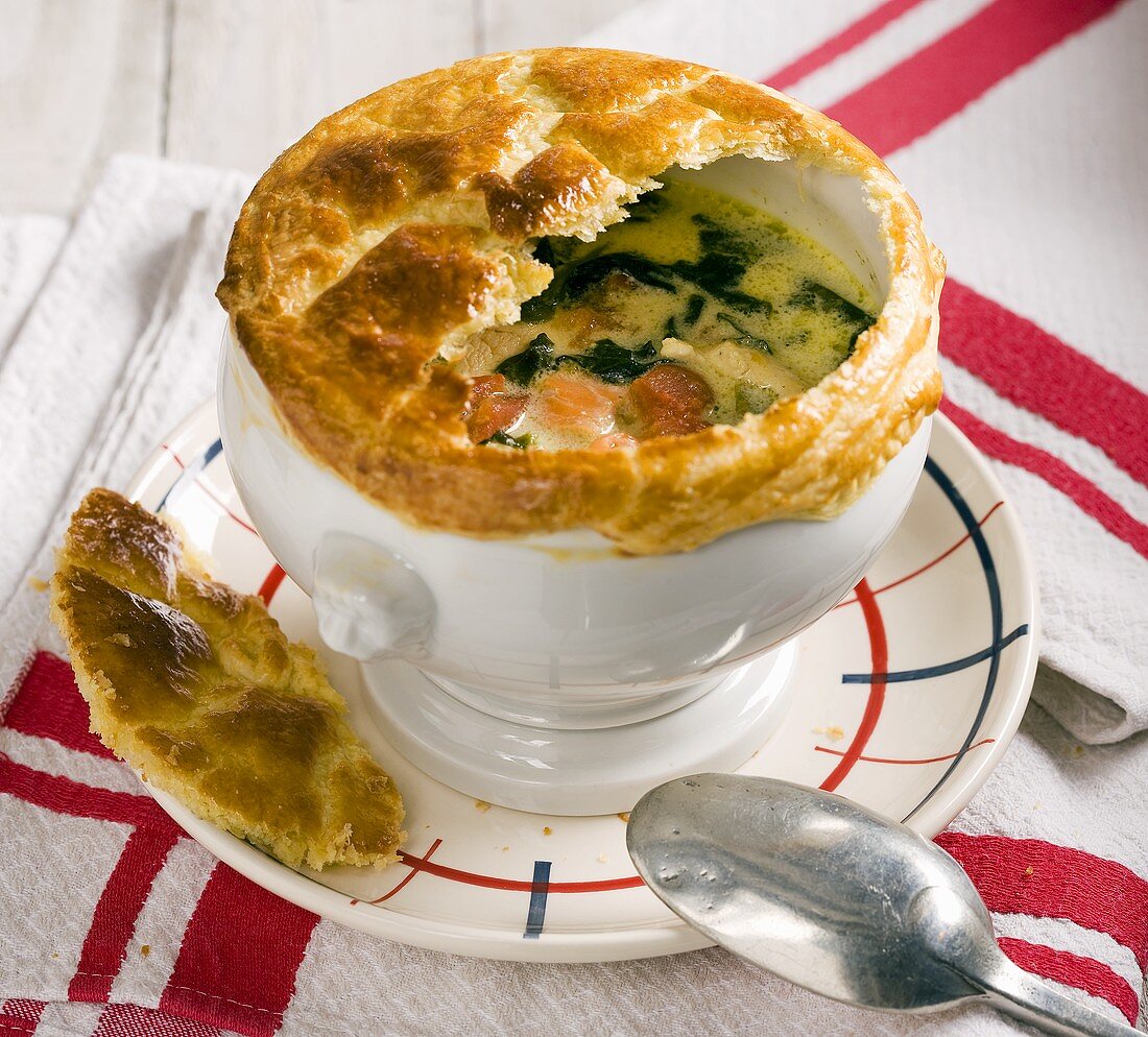 Chicken soup with smoked salmon, spinach and a puff pastry lid
