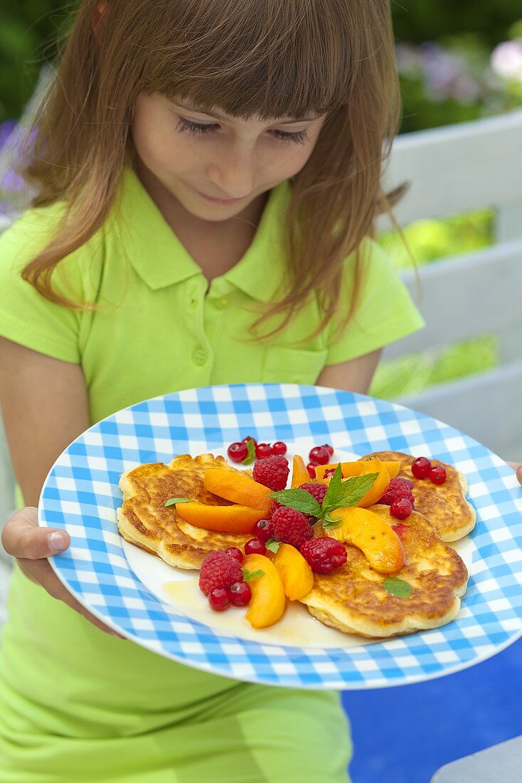 A girl holding a plate of pancakes and fresh fruit