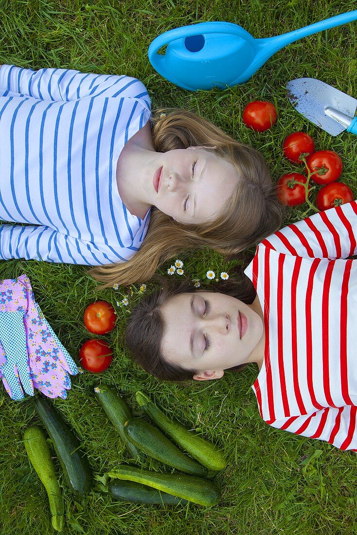 Two girls lying on the grass surrounded by vegetables