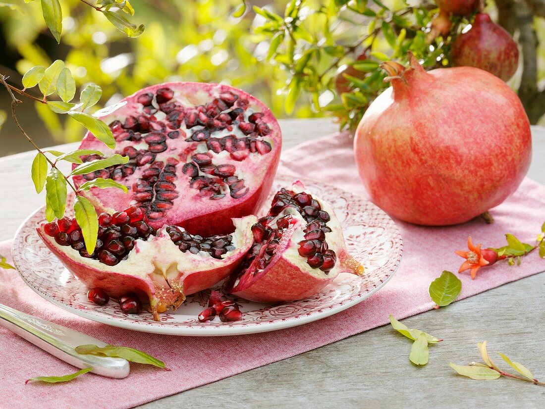 Aufgeschnittener Granatapfel auf Teller, daneben ganze Frucht