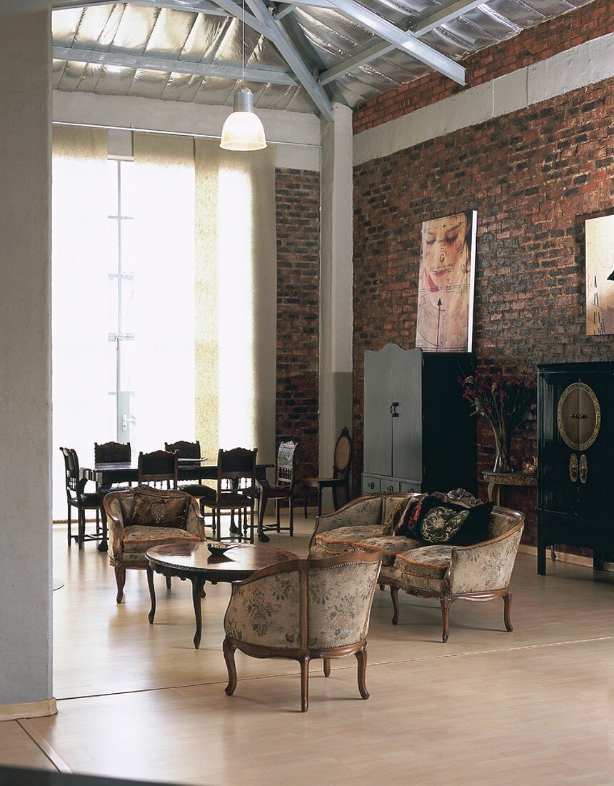 Open-plan living-dining room in loft apartment with period furniture, rough brick walls and exposed roof structure