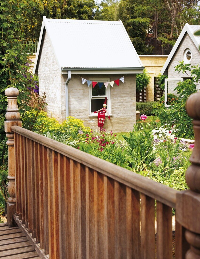 Shed decorated with colourful bunting behind garden flowers and wooden bridge