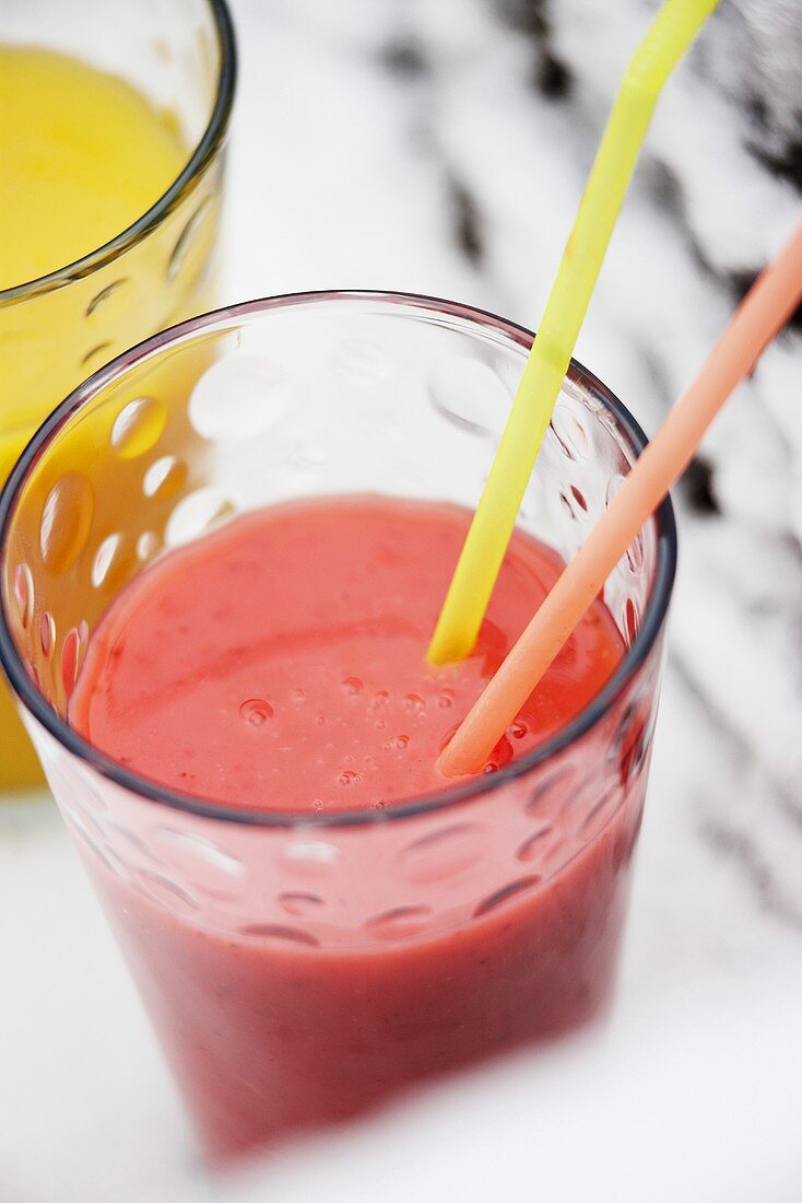 A glass of strawberry smoothie with straws