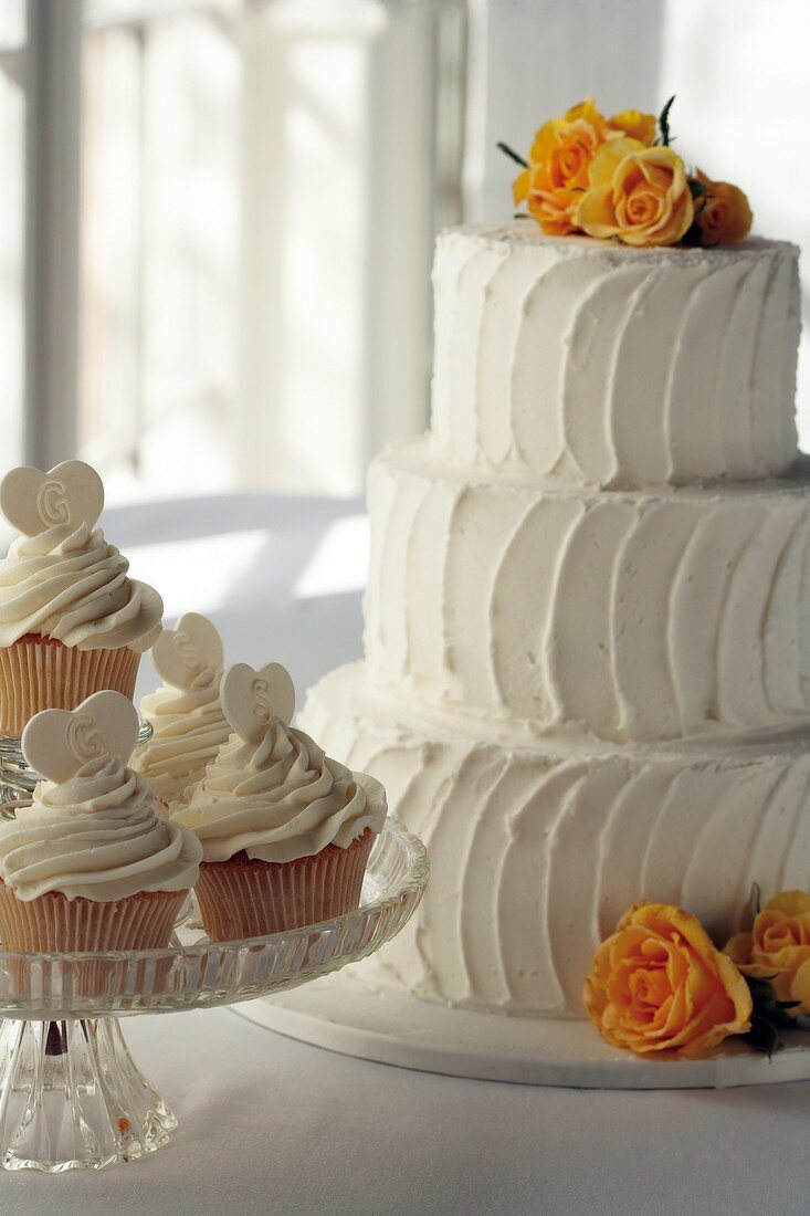 Dreistöckige weiße Hochzeitstorte und Zitronen-Cupcakes
