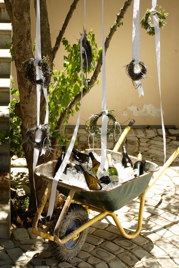 Small wreaths hanging above wheelbarrow holding ice cubes & wine bottles