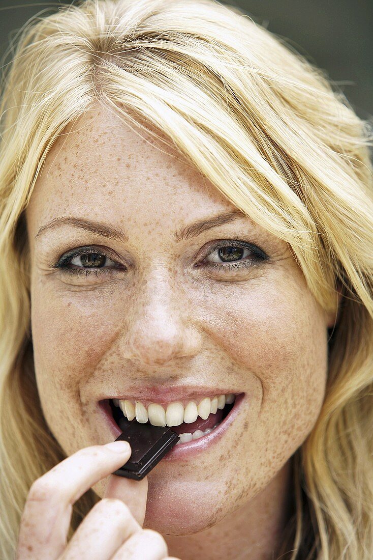 Blonde Frau isst ein Stück Schokolade