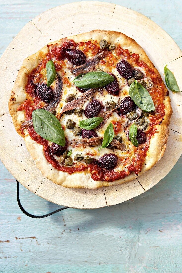 Pizza mit Anchovis, schwarzen Oliven und Basilikum