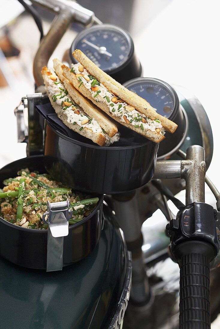 Bohnen-Quinoa-Salat & Sandwich mit Sardinencreme im Essensträger auf einem Motorrad