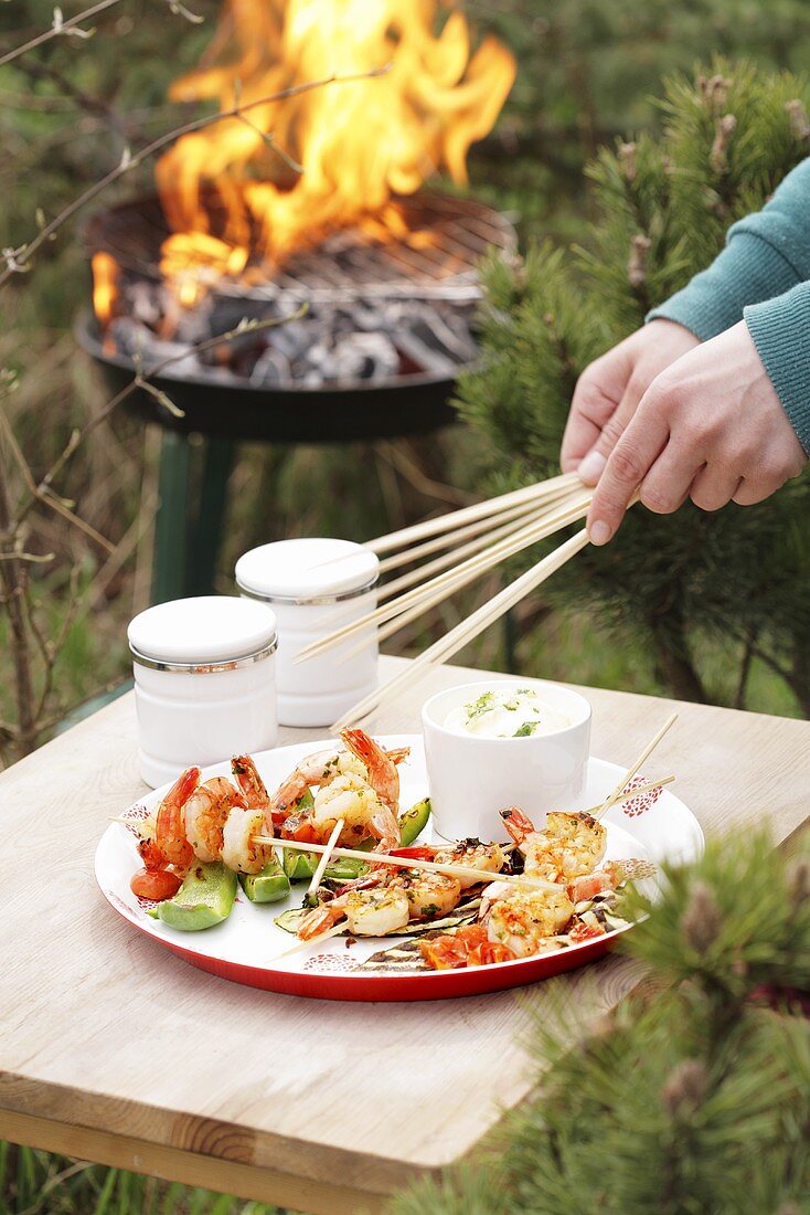 Barbecued prawn skewers on wooden table beside barbecue