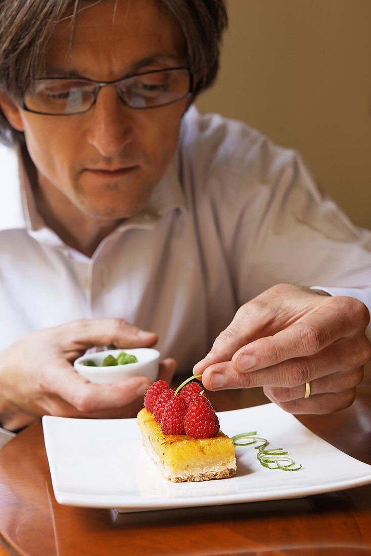 Man garnishing lemon slice with raspberries and lemon zest