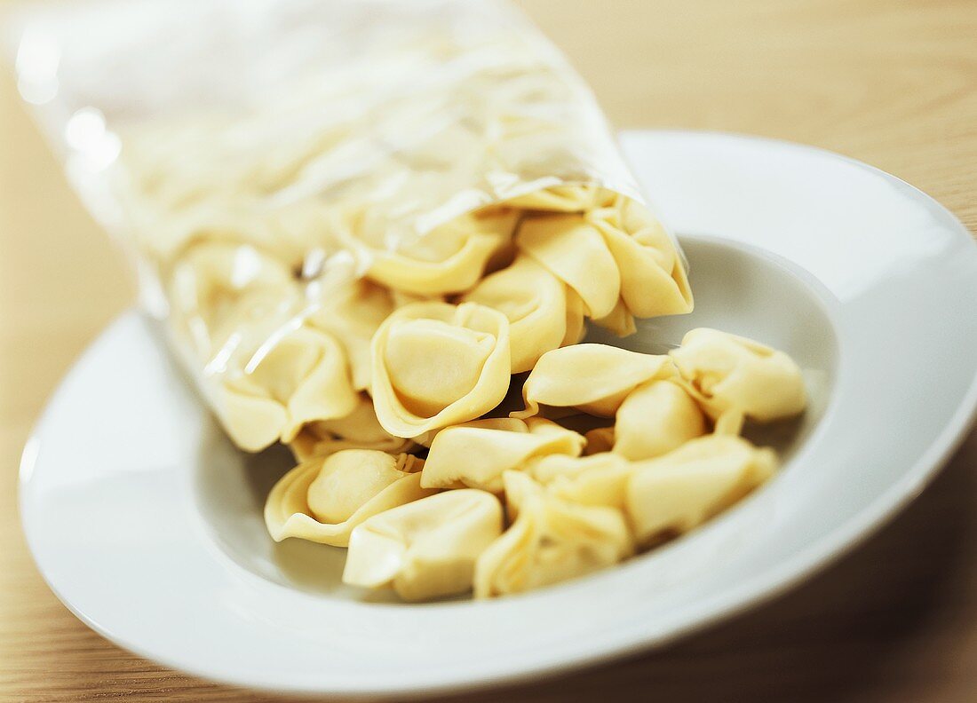 Tipping uncooked tortellini out of packaging onto plate