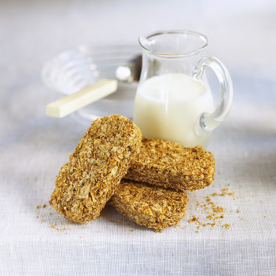 Three wheat biscuits (Weetabix) in front of a carafe of milk