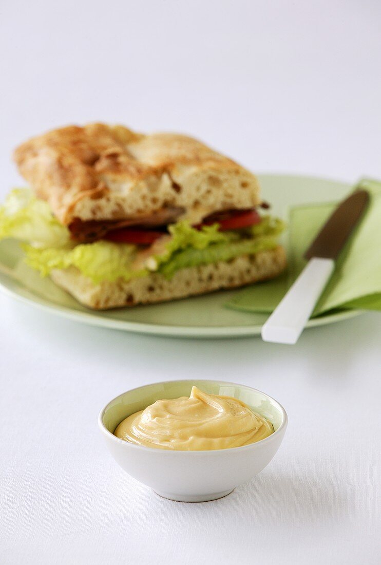 Mayonnaise in a small bowl in front of a sandwich