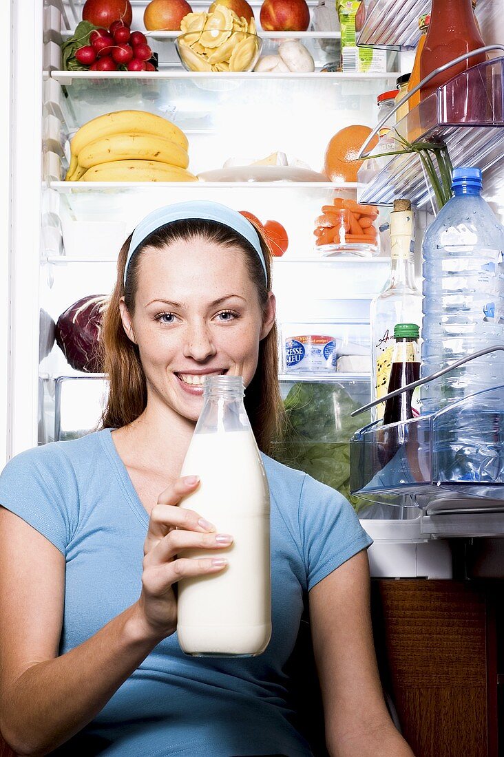 Junge Frau mit Milchflasche vor geöffnetem Kühlschrank