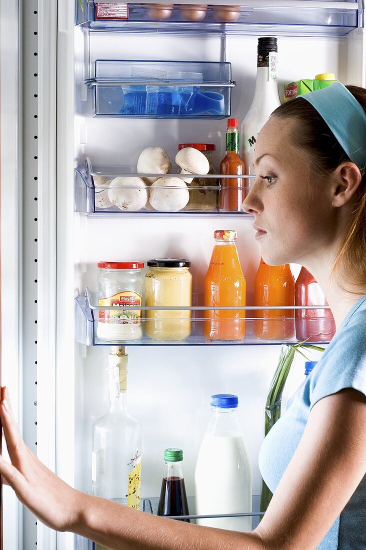 Junge Frau betrachtet kritisch Inhalt des Kühlschranks
