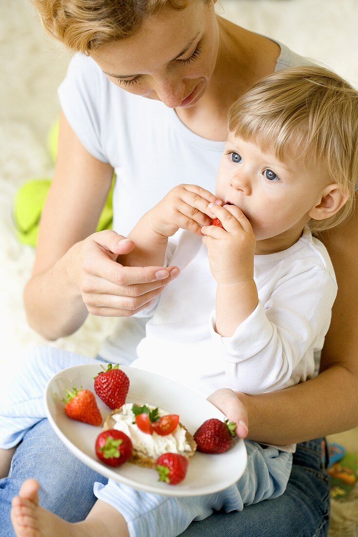 Kleines Kind isst mit Mutter Erdbeeren