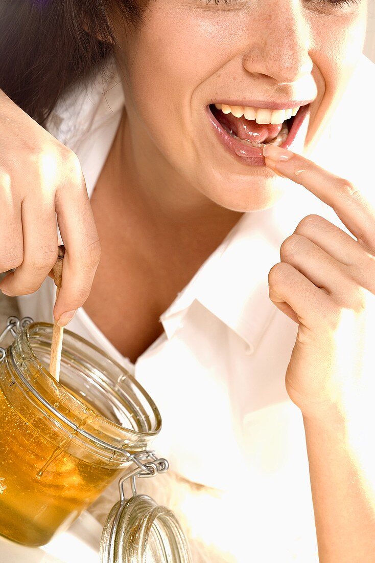 Young woman putting honey on her lips