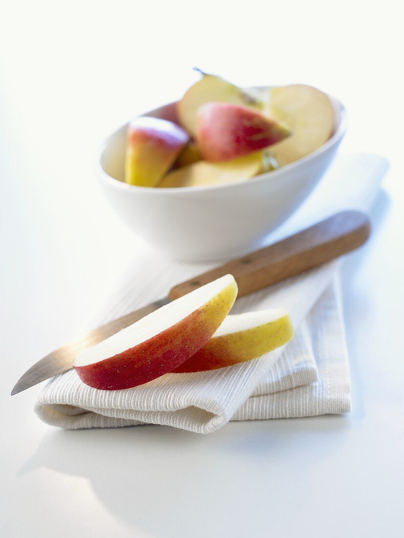 Apfelspalten und Küchenmesser vor Schale mit Apfelspalten