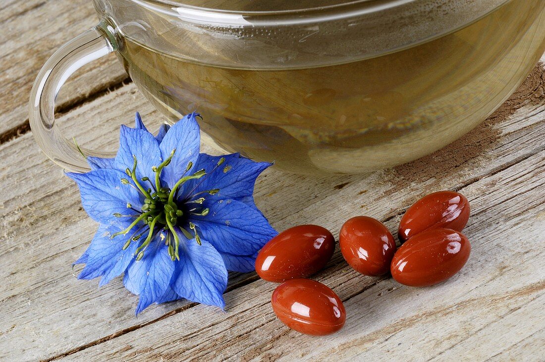 Love-in-a-mist flower beside black cumin capsules