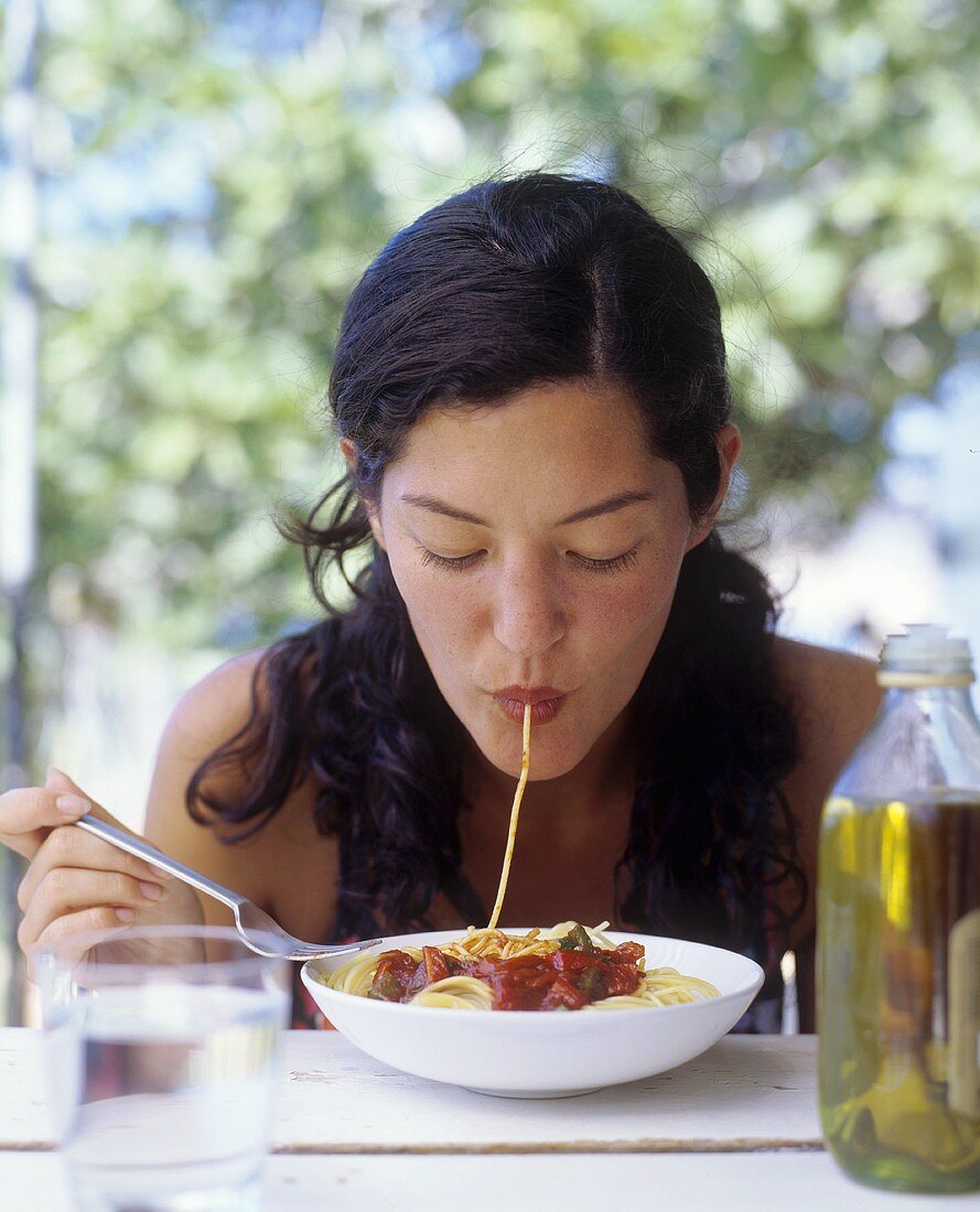 A woman sucking spaghetti into her mouth