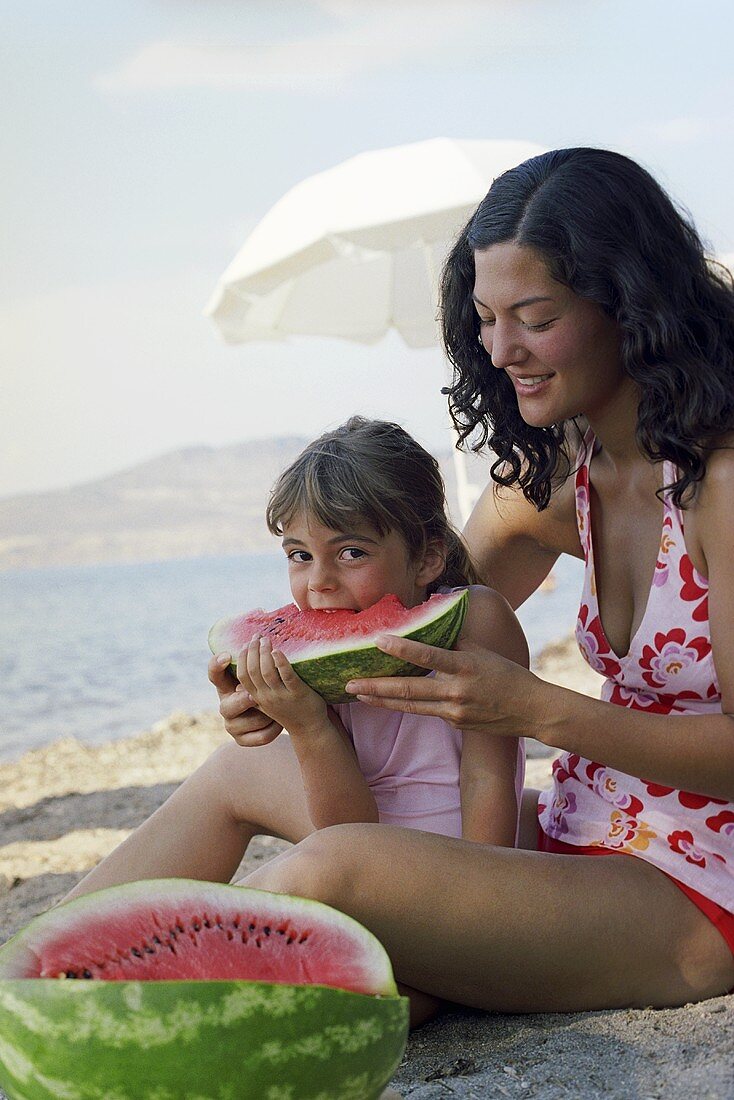 Mother and daughter eating watermelon on beach