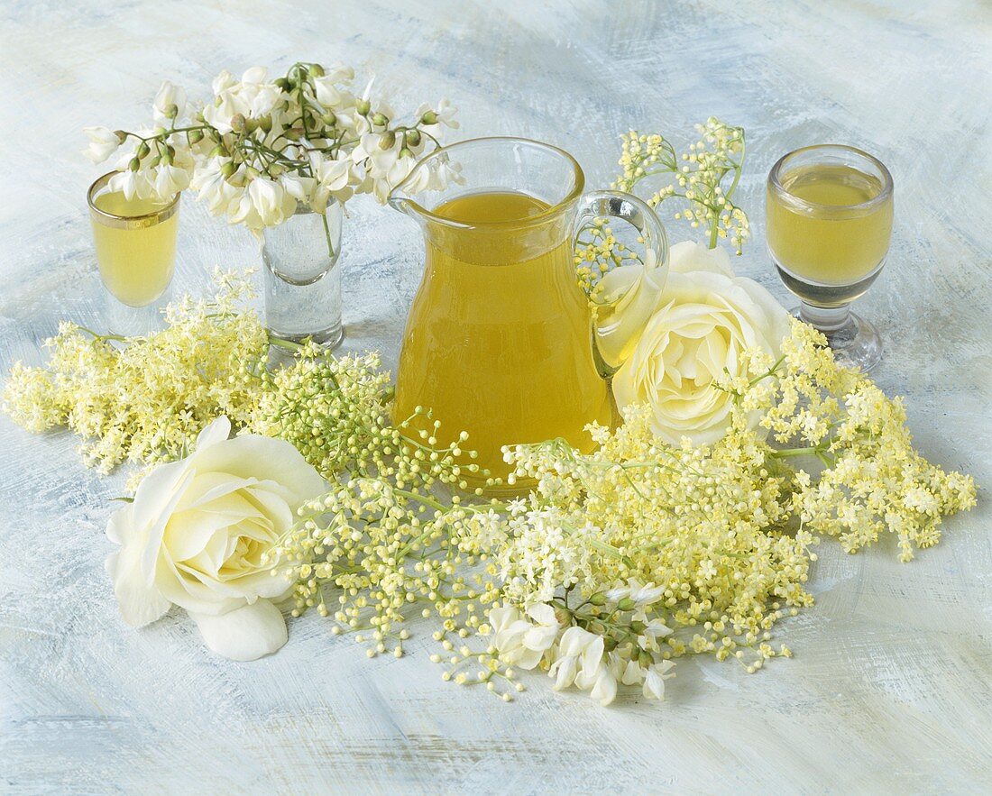 Elderflower drink in a carafe beside elderflowers and roses