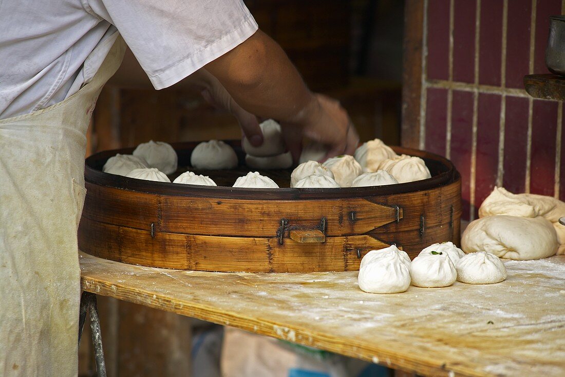 Asian pastry parcels being placed in giant steaming basket